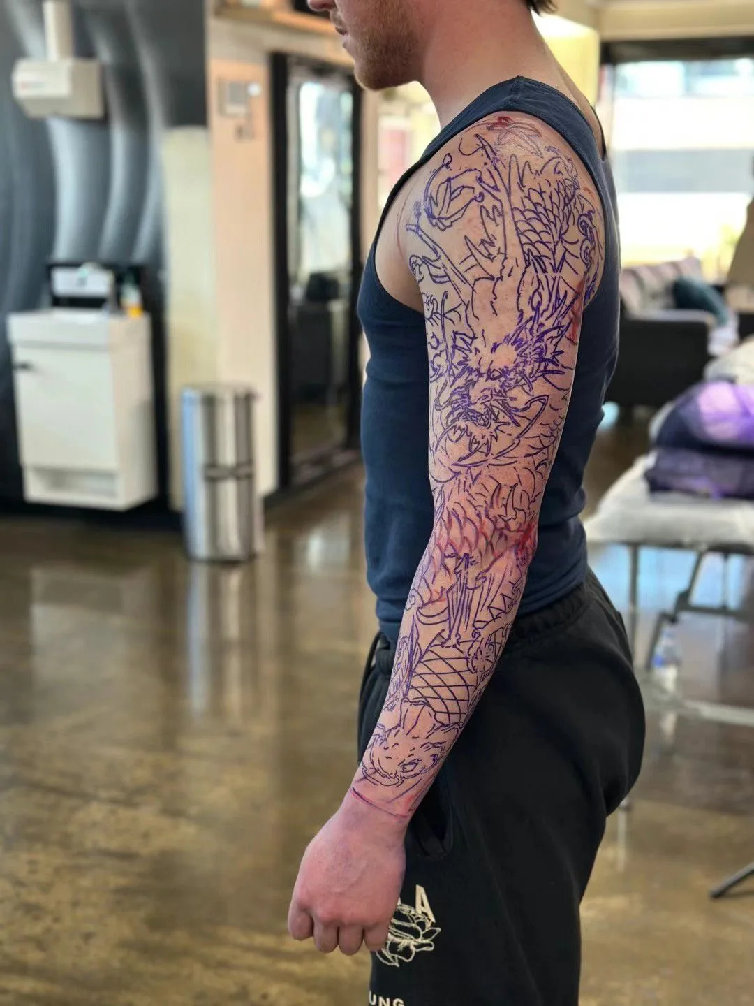A client with a fresh purple-stencil dragon sleeve, polished studio floor and reception visible