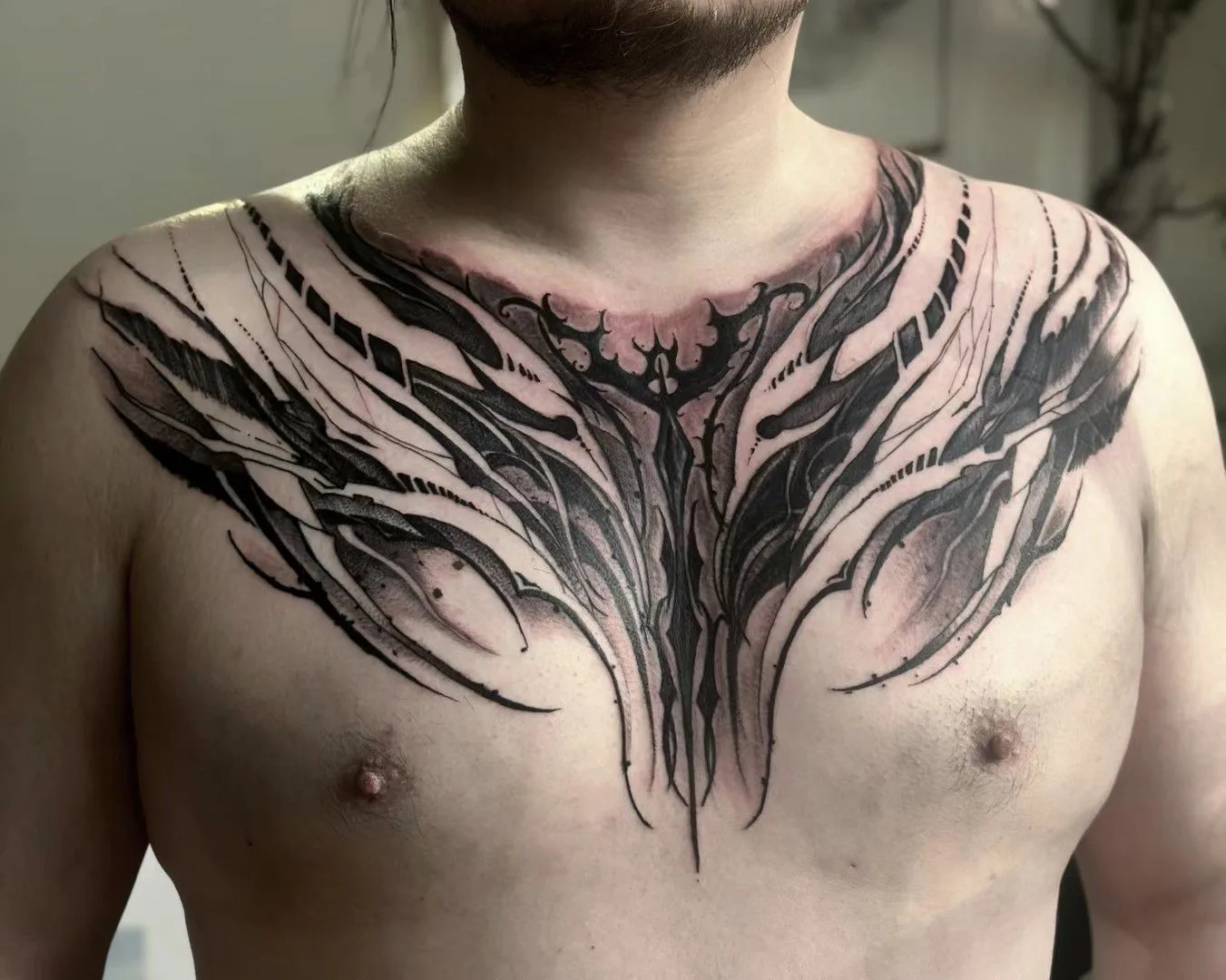 Black-and-grey biomechanical winged chest piece across a man's upper chest